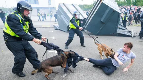 Joel Goodman/LNP A police officer with a police dog is controlling the dog who is biting on to a young person's trousers. A second police officer is also controlling a second police dog which is on the torso the young person.