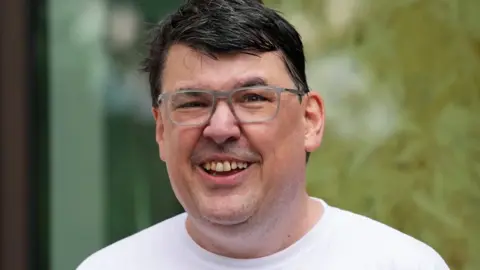 Graham Linehan smiling and wearing a white T-shirt outside court