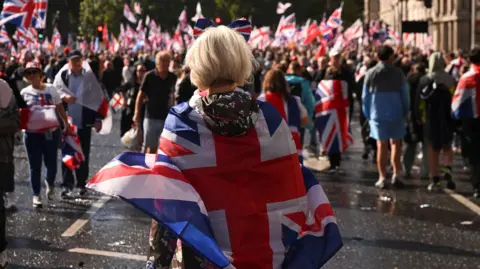 Reuters, una mujer que lleva una bandera de Union Jack sobre ella, asiste a un rally con personas que llevan banderas en la multitud frente a ella