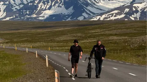 Handout A general view of Jack Pitcher walking up a mountain, with Jeremy Field walking next to him pushing a bike.