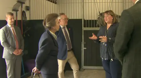 The Princess Royal (left) in blue jacket, with grey hair, beside man in blue jacket, grey hair and glasses. To the right, is Dr Esther Skelly-Smith, a woman with brown hair and striped black jacket.
