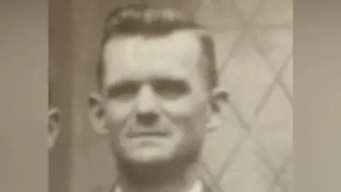 Family A close-up grainy black and white image of a man with dark hair who is looking at the camera.