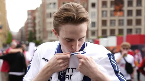 A Tottenham Hotspur fan kisses the club crest on his white replica shirt.