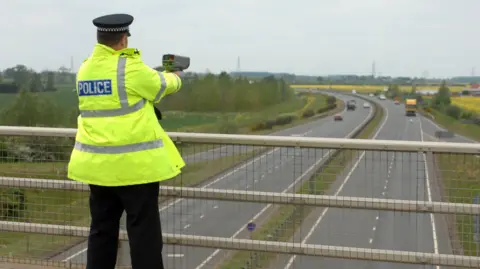 Getty Images A police officer conducts a speed camera check over a dual carriageway
