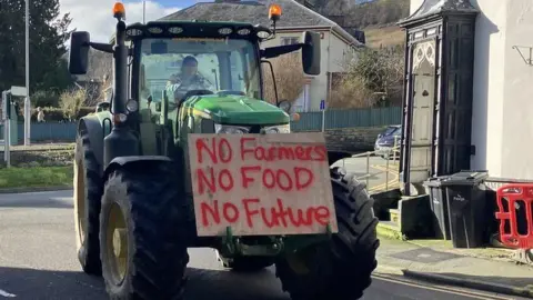 Farmer in tractor with a plaque saying "No farmers, no food, no future"