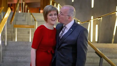 Getty Images A woman in a red dress standing next to a man with close cropped hair in a dark suit