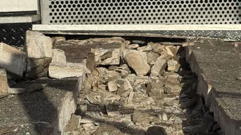 The damaged pavement, with a trench filled with smashed up concrete blocks.