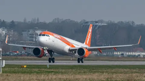 EasyJet/PA An EasyJet plane taking off from an airport runway. The plane has the airline's orange and white livery.