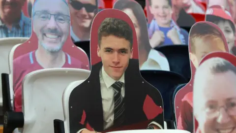 Getty Images A cardboard cut-out of a young man in a shirt, tie and blazer. He is surrounded by other cardboard cut-outs of fans.