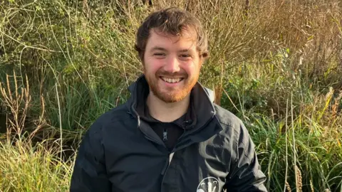 Ecologist Eric Swithinbank wearing an Avon Wildlife Trust top with plants and grass in the background