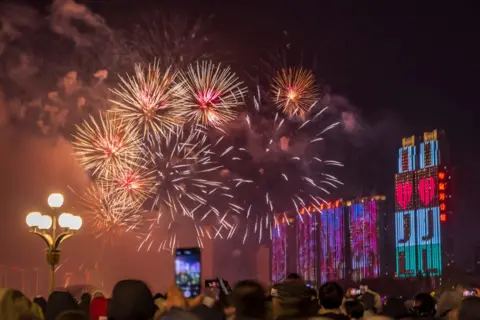 VCG melalui Getty Images Kembang api menerangi langit di atas Sungai Songhua saat pertunjukan kembang api menyambut Tahun Baru 2025 pada Malam Tahun Baru pada 31 Desember 2024 di Kota Jilin, Provinsi Jilin, Tiongkok. 