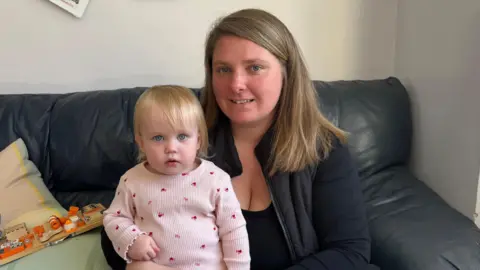 Mother and baby sat together on a sofa looking at the camera