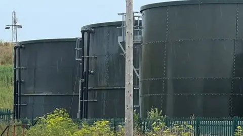 Three dark green waste tanks, owned by the company Transwaste