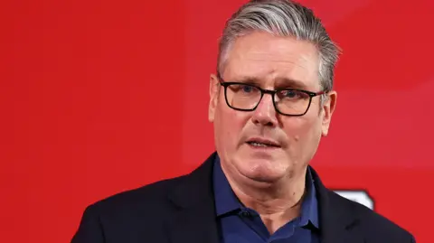 Reuters A serious-looking Sir Kier Starmer giving a speech. He is standing against a red backdrop, wearing a royal blue shirt open at the collar and a black blazer.