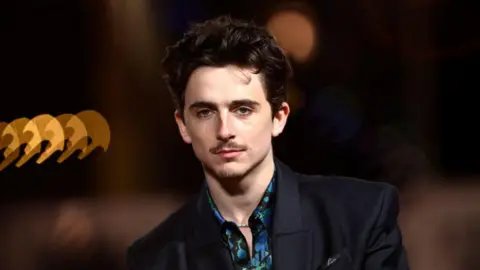 Getty Images A man in a black blazer and green and green shirt poses for the camera. 