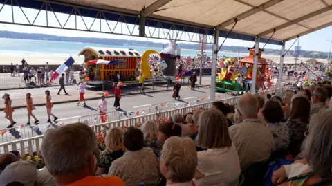 BBC Crowds gather on Victoria Avenue to watch a Jersey Battle of Flowers parade