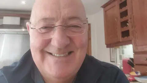 Robin Davies Robin Davies, bald-headed and wearing glasses and a black shirt, smiles and faces the camera in his kitchen