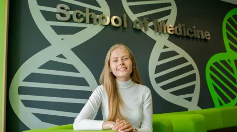 University of Sunderland Laura Giles, who has long blonde hair, smiling at the camera and sitting on a green couch.