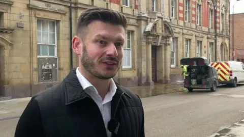 Keane Duncan standing in front of a man power washing the pavements to get rid of bird poo