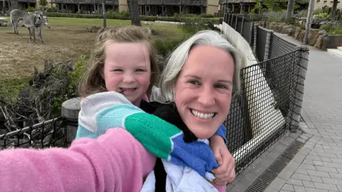 Elizabeth Bull A mother carrying a young child on her back. They are at the zoo and are both smiling. 