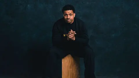 City of Wolverhampton Council Reepa dressed in all black and sat on a wooden block