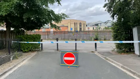 The exterior of the mosque building. There is blue and white police tape cordoning off the area and a red circle stop sign.