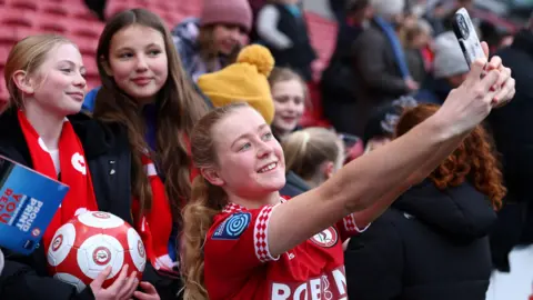 Getty Images Bristol City Women's FC player Mari Ward stretches out her arms so she can take a selfie with two young female fans at Ashton Gate after the game with Southampton.