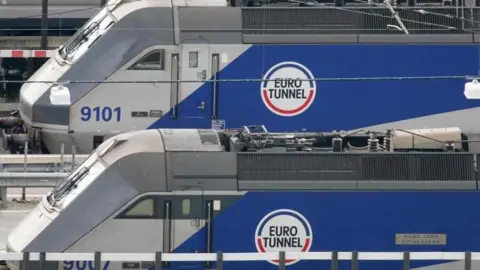 Two blue and white trains with the Eurotunnel logo are stood still on tracks