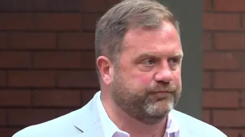 PA Media Grab from PA video of Warwickshire Police constable Robert Davies outside Birmingham Crown Court. He is wearing a pale grey jacket and white shirt and walking, with his face partially in profile. He has sort fair hair styleed to the side and a closely-cropped beard greying at the chin.