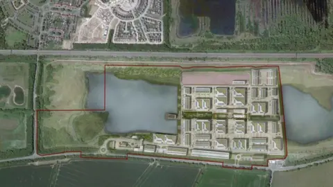 Quest Park An aerial view of a large development site outlined in red, set within a semi-rural landscape. To the right of the site, a planned complex of buildings is arranged in an orderly grid, with pathways, parking areas, and landscaped spaces between the structures. Several bodies of water, including a prominent lake on the left and smaller water features on the right, are integrated into the layout. Surrounding the site are fields, residential areas, and roads, indicating a transition between urban development and open countryside.