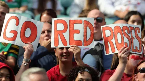 Fans hold up signs reading "GO RED ROSES" in bold red letters during a sporting event.