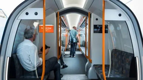 Getty Images The inside of a Glasgow Subway. A man sits on one of the seats which face each other along the long corridor of the vehicle. He looks at his phone and sits next to a sign which says the next stop is Buchanan Street