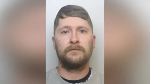 CTPNE Mugshot of Crowther. he has a short thick brown beard and short light brown hair swept over his head.