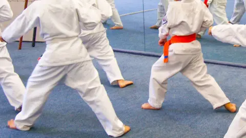 BBC children dressed in karate gear in a classroom with a mirror all the way along the back wall