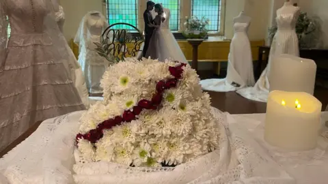 Flowers with dresses behind and candles next to them