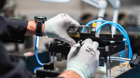 TMT First Close up of an engineer in grey gloves working at a bench on a piece of equipment.