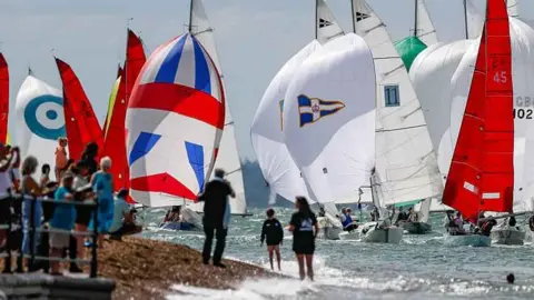 North Sails Cowes Week People line a beach as a fleet of sailing boat head towards the finish line off Cowes.