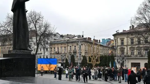 The city of Lviv, pictured from what appears to be a town square. A Ukraine flag is visible amid a crowd of people.