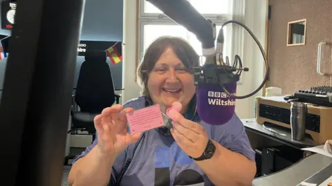 A woman holds a small pink duck in front of a microphone which says BBC Radio Wiltshire