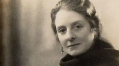 A sepia photograph of a woman with a scarf and earrings. 
