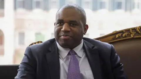 Reuters David Lammy with short dark hair wearing a grey suit and purple tie