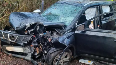 SCAS A crashed car on the side of the road. The front is mangled.