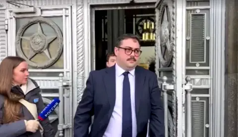 Reuters A man, dressed in a suit with a blue tie and wearing dark-rimed glasses, leaves building with ornately decorated doors