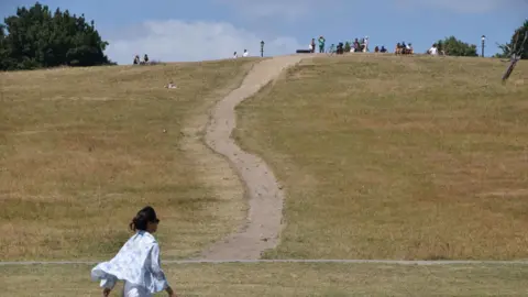 A woman walks along a dry Primrose Hill