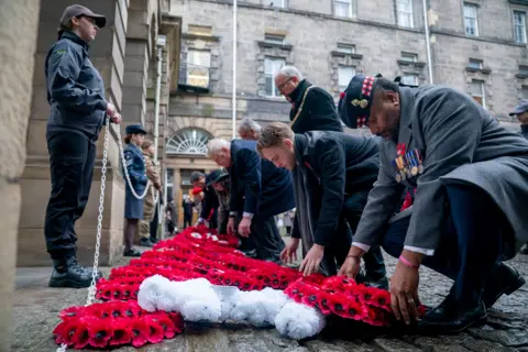 Getty Images People lay red poppy wreaths during a Remembrance Sunday ceremony at the Stone of Remembrance outside the City Chambers in Edinburgh.