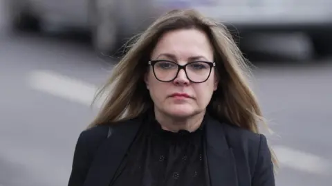 A woman wearing glasses and a black suit.
