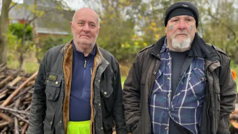 Harvey Bell/BBC Colin Cripps and Stephen St Claire standing in front of a wood pile.