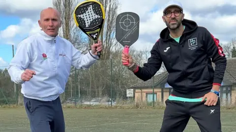 Alan Jordan Alan wearing a white track suit jacket and grey trousers and Pep wearing a black track suit- both holding padel tennis rackets 