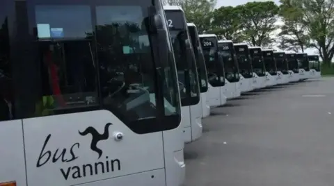 A row of single-decker silver buses in a semi-circle, They have dark tinted windows and the Bus Vannin logo on the side.