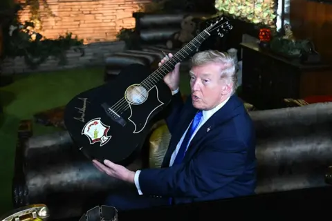 AFP via Getty Images US President Donald Trump holds up a guitar with his signature on it during a visit to Elvis Presley's former home, Graceland, in Memphis, Tennessee, USA.